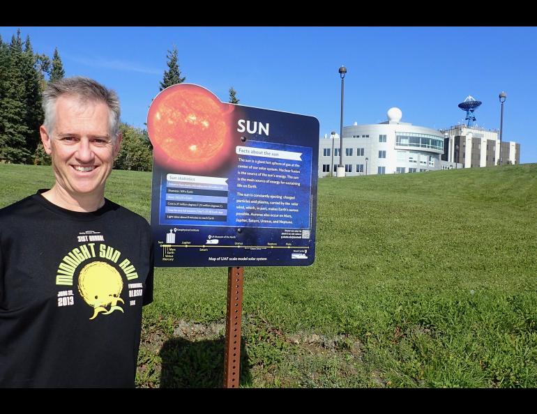 Peter Delamere pauses in front of a UAF Planet Walk sign at the University of Alaska Fairbanks, with the International Arctic Research Center and the Geophysical Institute in the background. Photo by Ned Rozell.