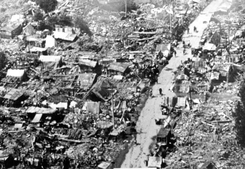 Debris of broken buildings, houses, etc. People walking on dirt streets.