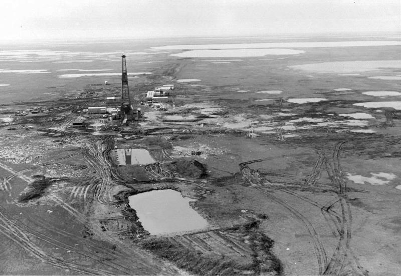 An oil tower amidst muddy and pool-filled dirt. 