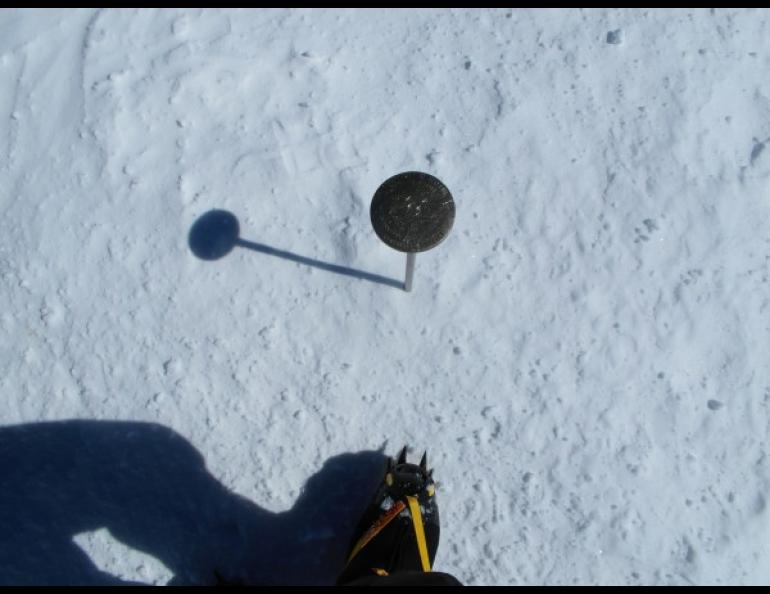 The official U.S. Geological Survey marker rests on the summit of Denali in 2013, with climber Ken Karstens’ foot for scale. Photo courtesy of The Centennial Climb.