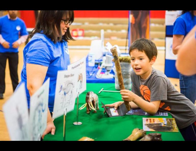 Margaret Cysewski, an outreach educator with the UAF Geophysical Institute, talks to a Tanana boy as he examines a 30,000-year-old willow stick from the Fox permafrost tunnel in 2016. UAF photo by JR Ancheta.