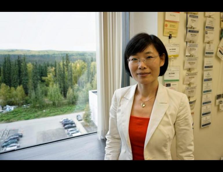 Hui Zhang, a physics professor and scientist studying the magnetosphere at the University of Alaska Fairbanks, stands in her office on the seventh floor of the Geophysical Institute. Her many conference badges hang on the wall behind her. Photo by Josh Hartman.