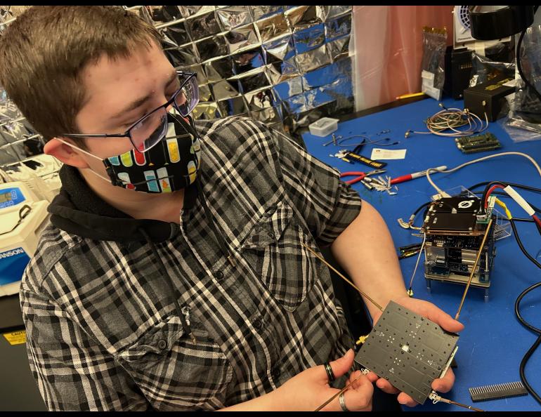 Student Caleb Fronek, the nanosat project manager, holds the retrodirective and UHF antennas. The avionics test stack is on the tabletop. Photo by Rod Boyce.