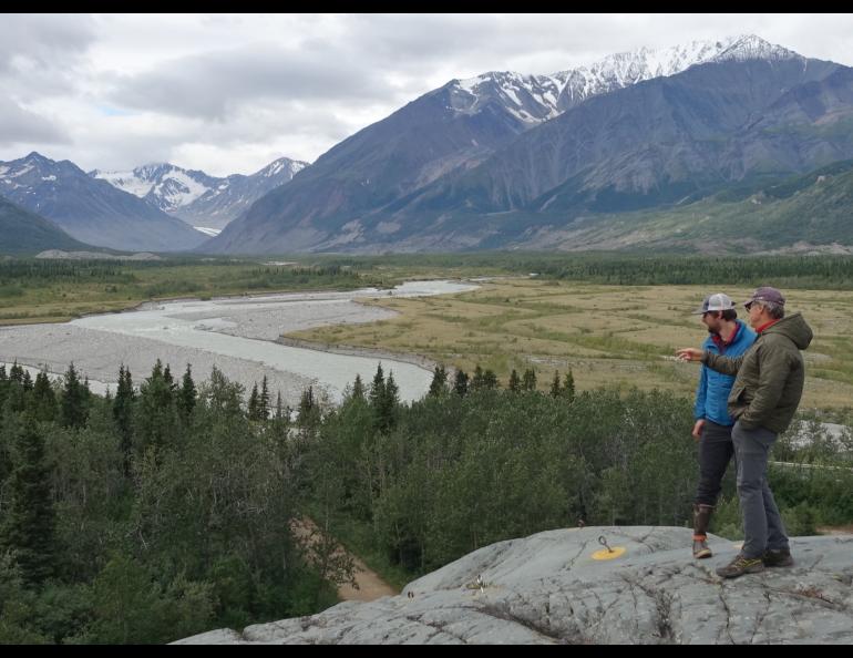 Phillip Wilson (blue jacket) and Dan Mann stand on a rock outcrop that was scoured by floodwaters a few centuries ago when Black Rapids Glacier — far in the distance — advanced to dam the Delta River. Photo by Ned Rozell.