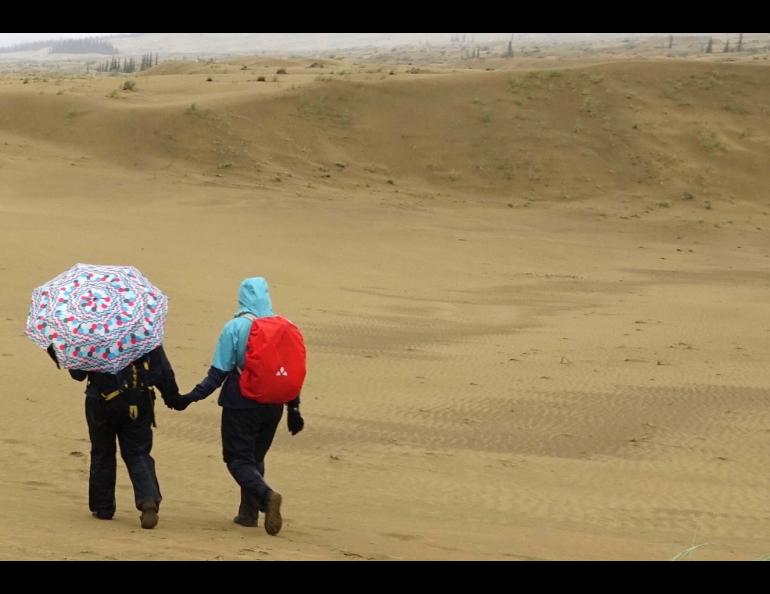 Karin Bodony, left with umbrella, hikes with her 15-year-old daughter Ida in the Nogahabara Dunes 35 miles west of Huslia. Photo by Ned Rozell.