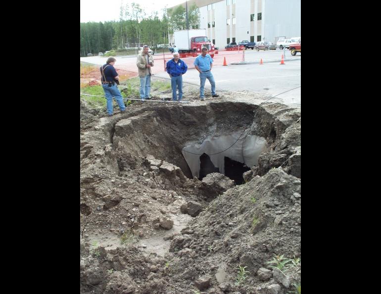 Workers gather around a thermokarst — a hole that opened up due to thawing permafrost beneath — behind a University of Alaska Fairbanks building. Photo by Vladimir Romanovsky.