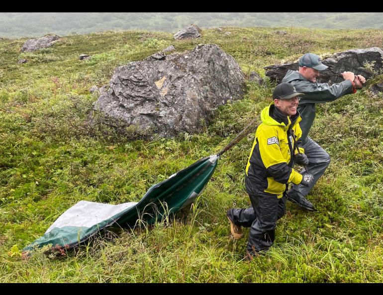 Gerry Hatcher, left, and Drake Singleton drag a deflated boat pontoon over wet vegetation to reach Allison Lake near Valdez. Photo by Ned Rozell.