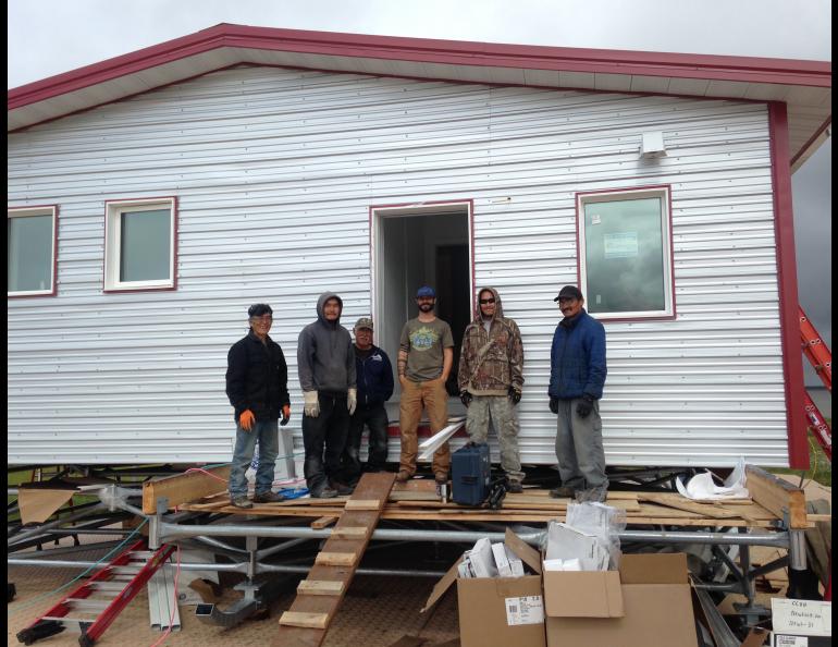 Aaron Cooke, in the T-shirt and blue hat, poses in front of an efficient house he helped design after he and Newtok residents built it at the new village site of Mertarvik in 2016. Photo by Molly Rettig. 