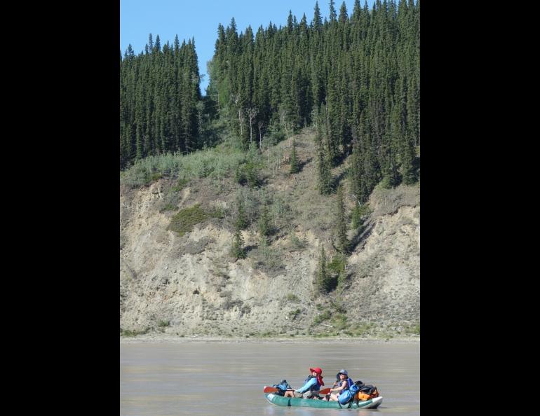 Two boaters on the Yukon River cross from the Yukon into Alaska on July 5, 2019. The border is marked by a 20-foot clearing and a metal obelisk. Photo by Ned Rozell.