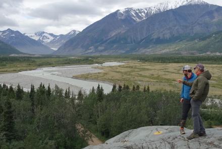 Phillip Wilson (blue jacket) and Dan Mann stand on a rock outcrop that was scoured by floodwaters a few centuries ago when Black Rapids Glacier — far in the distance — advanced to dam the Delta River. Photo by Ned Rozell.