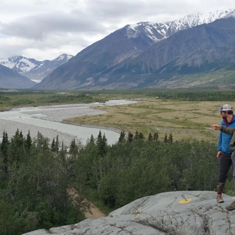 Phillip Wilson (blue jacket) and Dan Mann stand on a rock outcrop that was scoured by floodwaters a few centuries ago when Black Rapids Glacier — far in the distance — advanced to dam the Delta River. Photo by Ned Rozell.